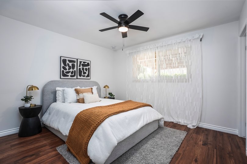 Bedroom with dark wood floors, a grey upholstered bed frame, and white walls featuring a black ceiling fan at 5237 Diane Ave in Clairemont.