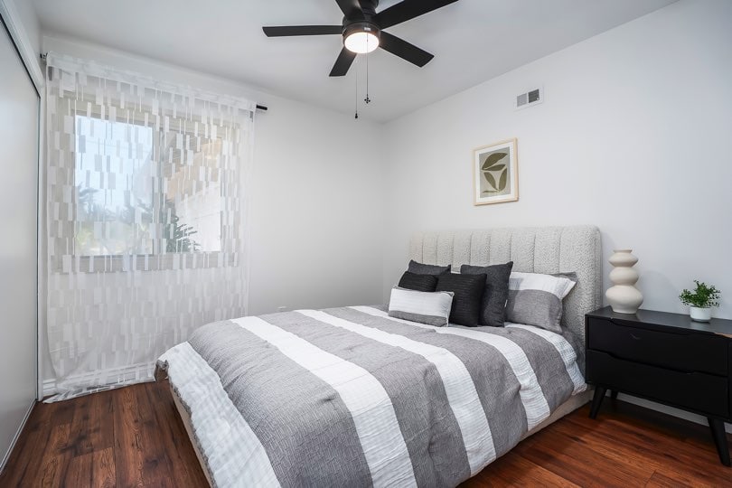 Bedroom with dark wood floors, a grey upholstered bed, and a black nightstand beneath a black ceiling fan at 5237 Diane Ave in Clairemont.
