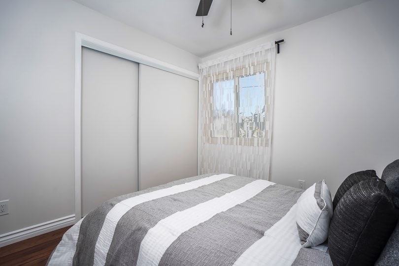 Bedroom featuring a sliding closet door, a window with white curtains, and a bed with grey and white striped bedding at 5237 Diane Ave in Clairemont.
