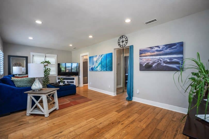 Open living space with wood floors, light grey walls, blue seating area, and ocean-themed wall art at 3381 Bancroft St in North Park.