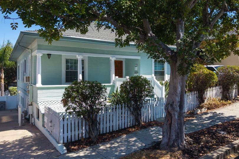 A light mint-green craftsman bungalow with a full-width front porch supported by columns is situated behind a white picket fence at 1932 C Street in Golden Hill.