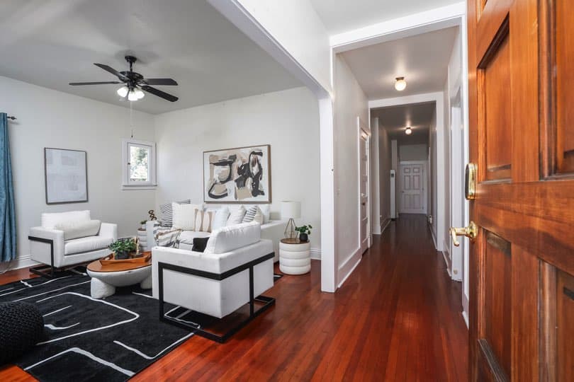 A living room with white armchairs, a couch, and a dark patterned rug is viewed from the entryway with a hardwood floor and hallway at 1932 C Street in Golden Hill.