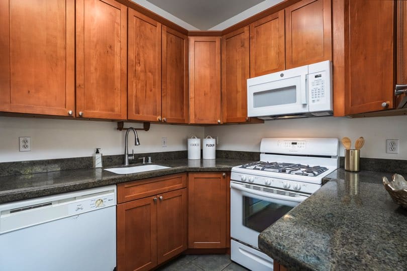 A kitchen with wooden cabinets, dark granite countertops, a white oven, and a dishwasher at 1932 C Street in Golden Hill.