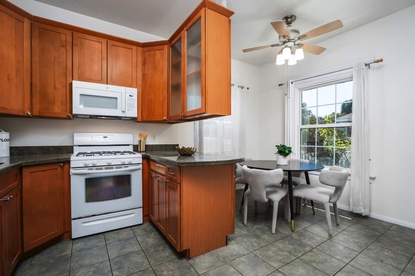 A kitchen with wood cabinets, white appliances, and a dining table by the window at 1932 C Street in Golden Hill.
