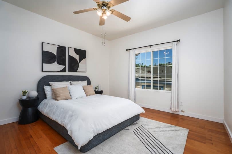 A bedroom with a dark upholstered bed, white linens, a patterned rug, and a window with white curtains at 1932 C Street in Golden Hill.