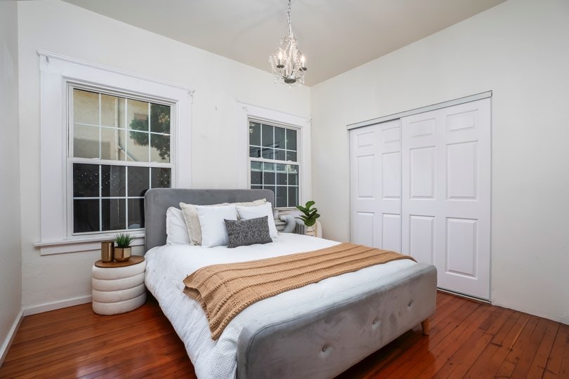 A bedroom with a gray upholstered bed, white linens, a brown throw blanket, windows, and white closet doors at 1932 C Street in Golden Hill.
