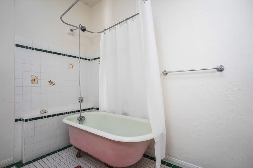 A pink clawfoot bathtub with a wrap-around shower curtain is positioned against a tiled wall at 1932 C Street in Golden Hill.