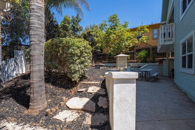 A stone patio area with a picnic table sits alongside a landscaped yard with mulch and a palm tree at 1932 C Street in Golden Hill.