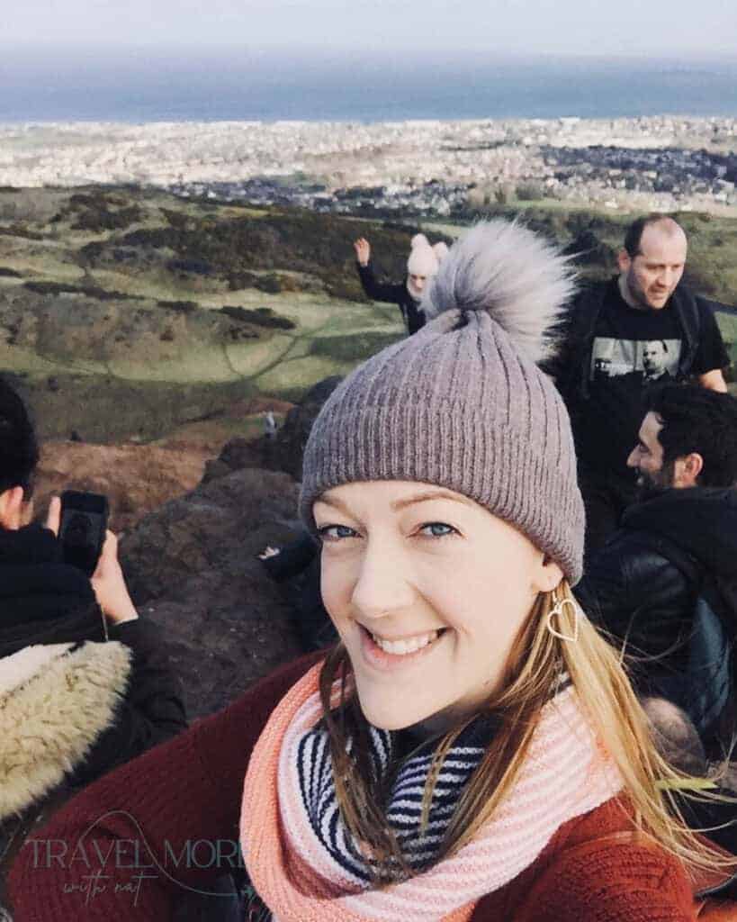 Traveller smiling on Arthur’s Seat with panoramic views across Edinburgh and the coastline in the background.