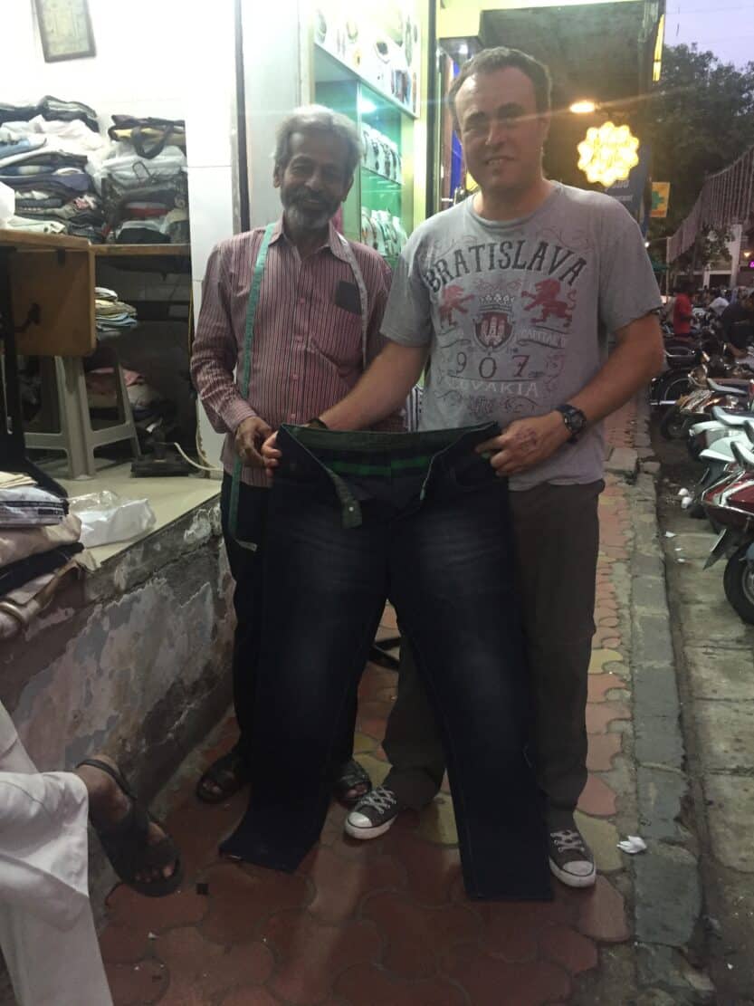 Street Tailor in Coloba in Mumbai, India Andy holding a pair of jeans up with street tailor in Coloba in Mumbai, India
