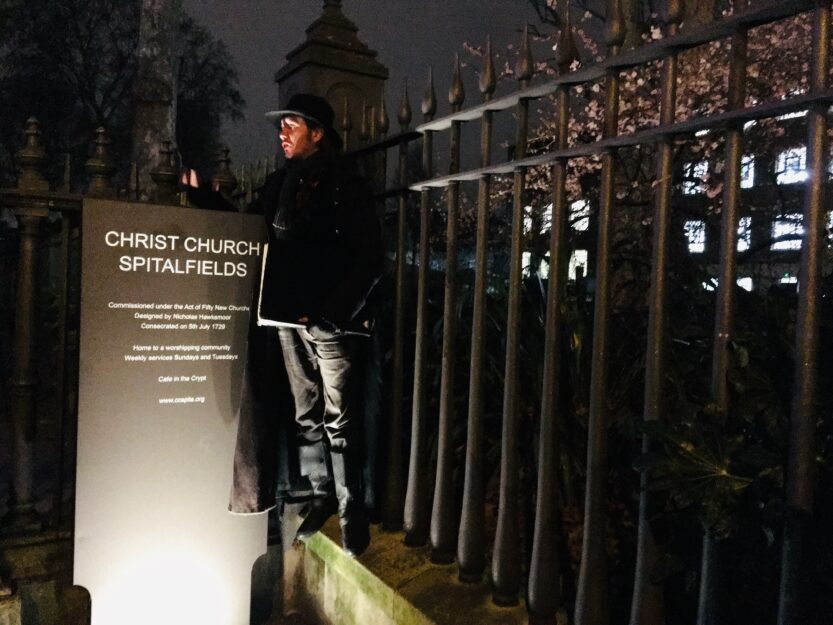 Jack the Ripper Tour London Nighttime Jack the Ripper Tour London. Guide standing near the lit Christ Church Spitalfields sign, in front of a black iron fence