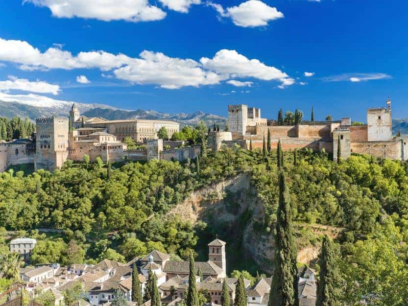 Alhambra in Granada, Spain Alhambra in Granada Spain. Stone palace with green trees in foreground and blue sky with white clouds in background.