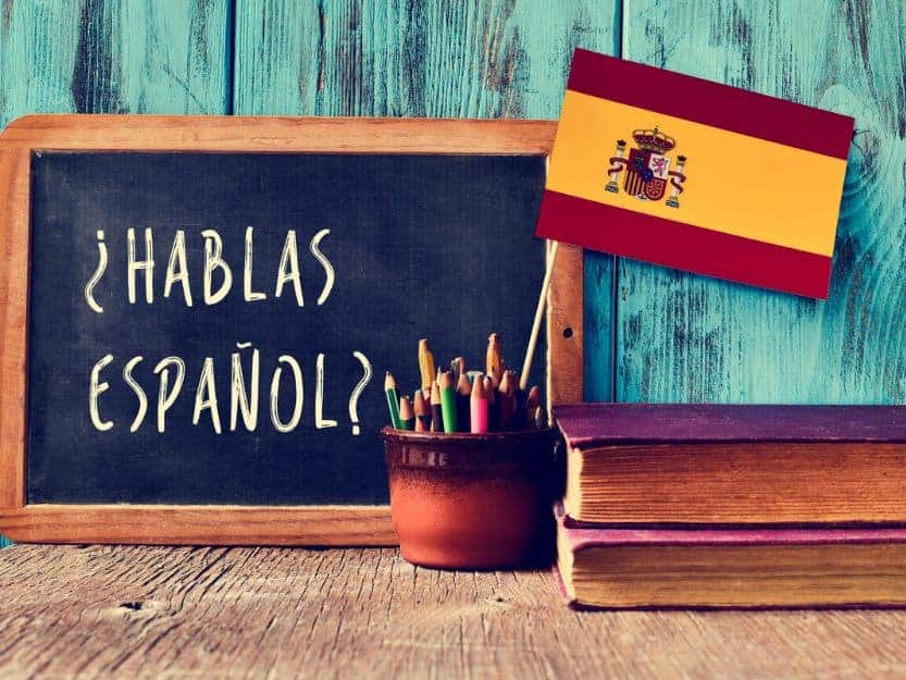 Do You Speak Spanish Sign Blackboard with Hablas Espanol - Do you speak Spanish? on it - with a Spanish flag to the right. Red, yellow and red horizontal stripe with Spain coat of arms