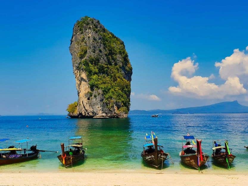 Fishing Boats and Limestone Karst on Railay Beach Fishing boats in foreground on Railay Beach with tree covered limestone karst cliff in the background surrounded by blue-green sea.