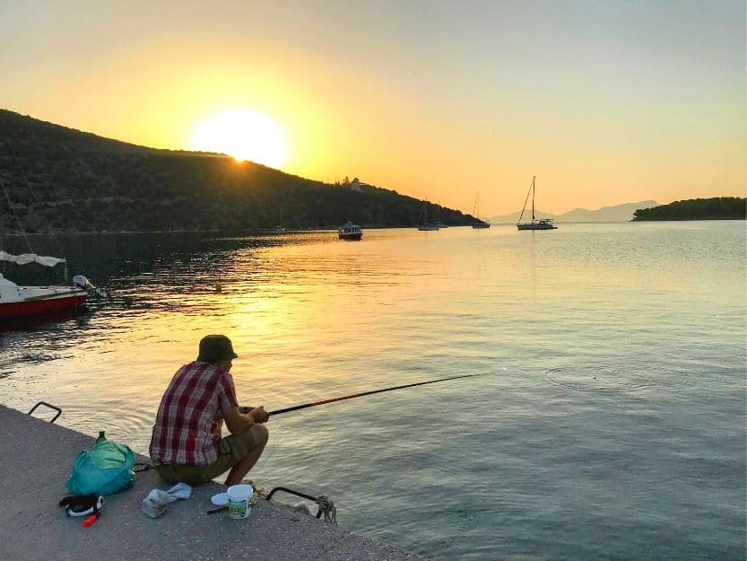 Fishing in Ermioni in Greece Andy fishing at sunrise, sitting on the port on Limani side of Ermioni. He is wearing a red and white checked shirt.