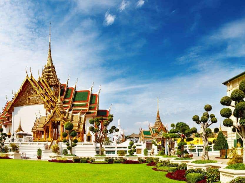 Grand Palace in Bangkok, Thailand Grand Palace in Bangkok, Thailand. White walls, green, gold and red roof, with green grass in foreground and blue sky in the background.