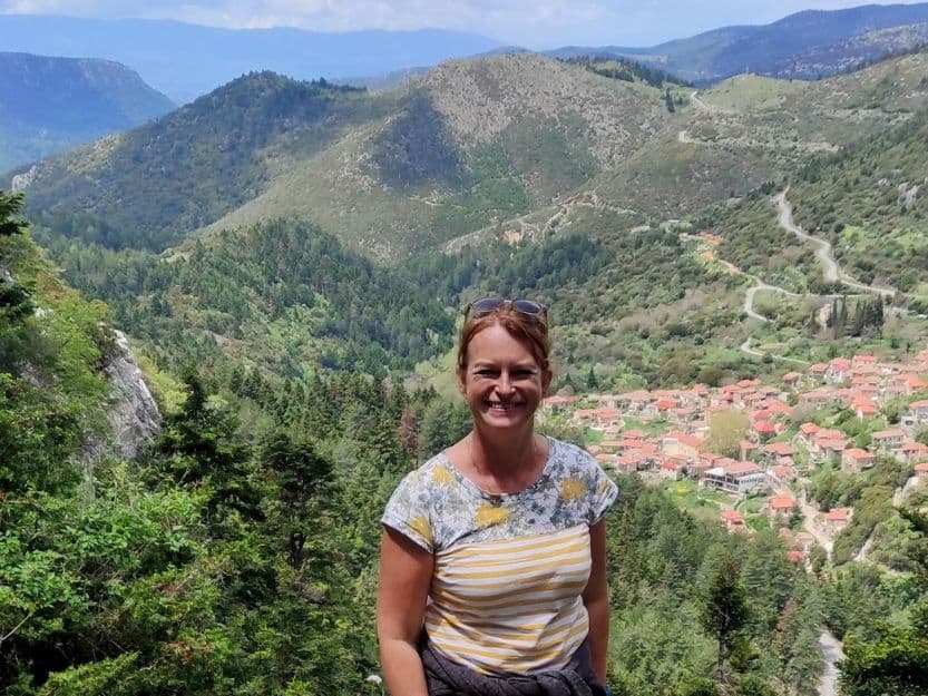 Hike to Agios Ioannis, Laconia Tanya standing with the view of Tsintzina village, the valley and mountains behind her on a short hike to Agios Ioannis in the Paronas Mountains, Laconia. She's wearing a white and yellow striped t-shirt and has her red hair tied back.