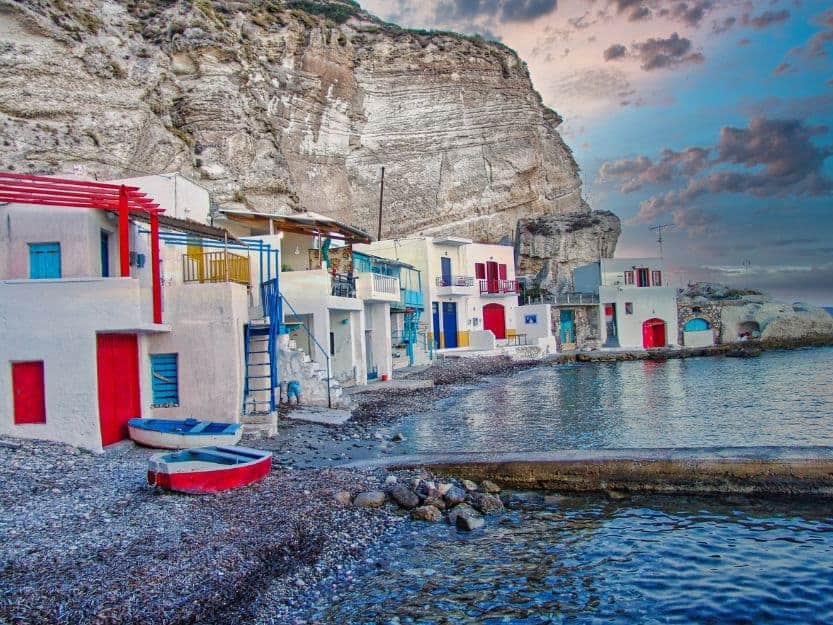 Klima Beach on Milos White and colourful Syrmatas (old fishing houses) on the pebbly Kilma Beach fishing village. Cliffs towering above on the left and calm sea on the right.