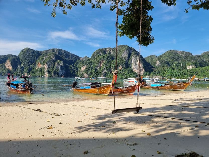 Maya Bay on Koh Phi Phi, Thailand Rope swing on beach in Maya Bay on Koh Phi Phi Island with fishing boats and limestone karst cliffs in the background.