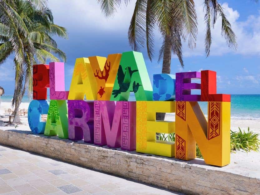 Playa del Carmen Sign Colourful Playa del Carmen sign with two palm trees, white sand beach and blue sea behind it.