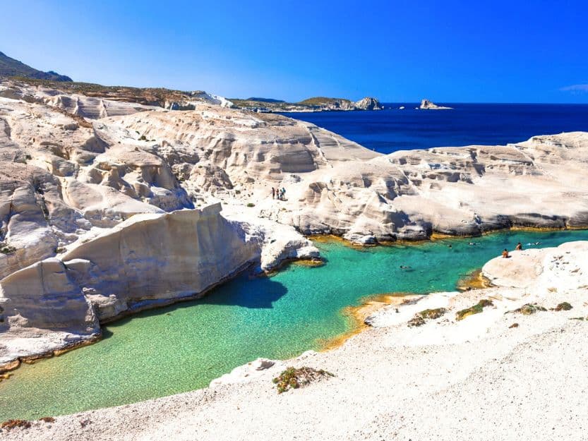 Sarakiniko Beach on Milos in Greece. Sarakiniko Beach on Milos in Greece. Lunar like light beige rocks, surrounding a clear turquoise blue swimming area with darker blue sea in the background and blue sky above.
