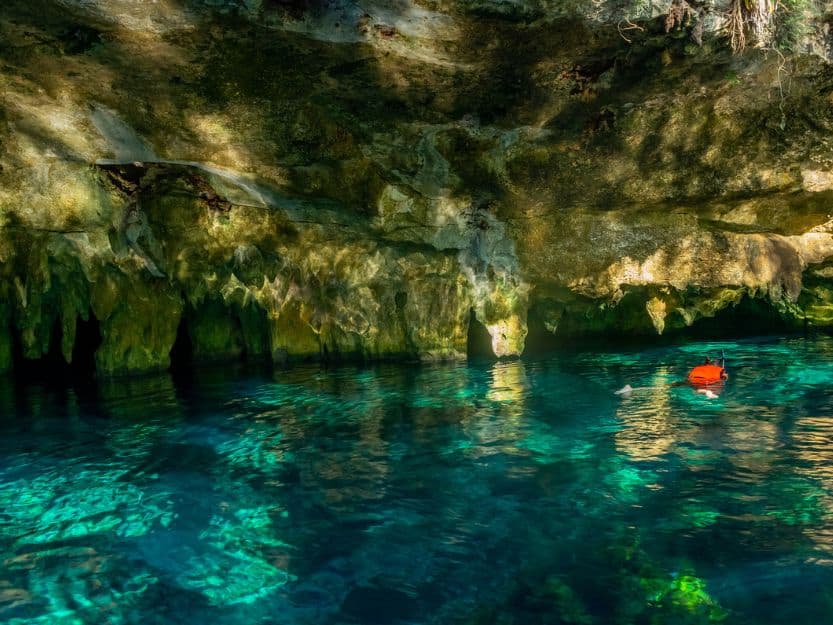 Swimming in Gran Cenote in Tulum, Mexico. Person wearing a red life jacket, snorkelling in the clear blue water of Gran Cenote in Tulum in mexico. The sinkhole also has stalagmites and stalactites.