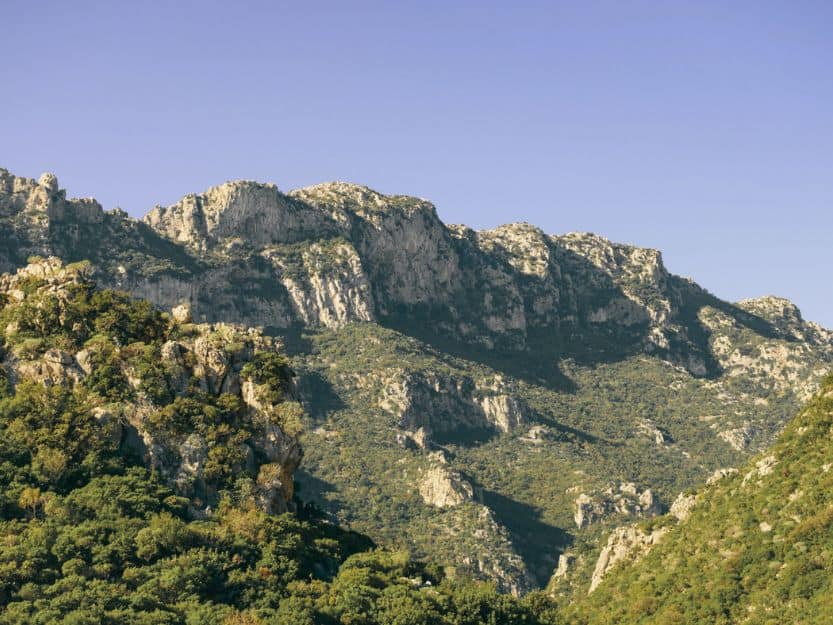 Taygetus Mountains Taygetus mountains in Laconia. Light grey limestone rock mountain range, covered in patches of green trees and bushes. Light blue sky in the background.