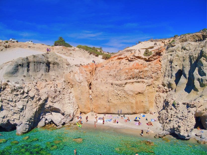 Tsigrado Beach on Milos Greece Tsigrado Beach on Milos Greece. Small sandy beach with bright blue sea surrounded by tall red stone cliffs.