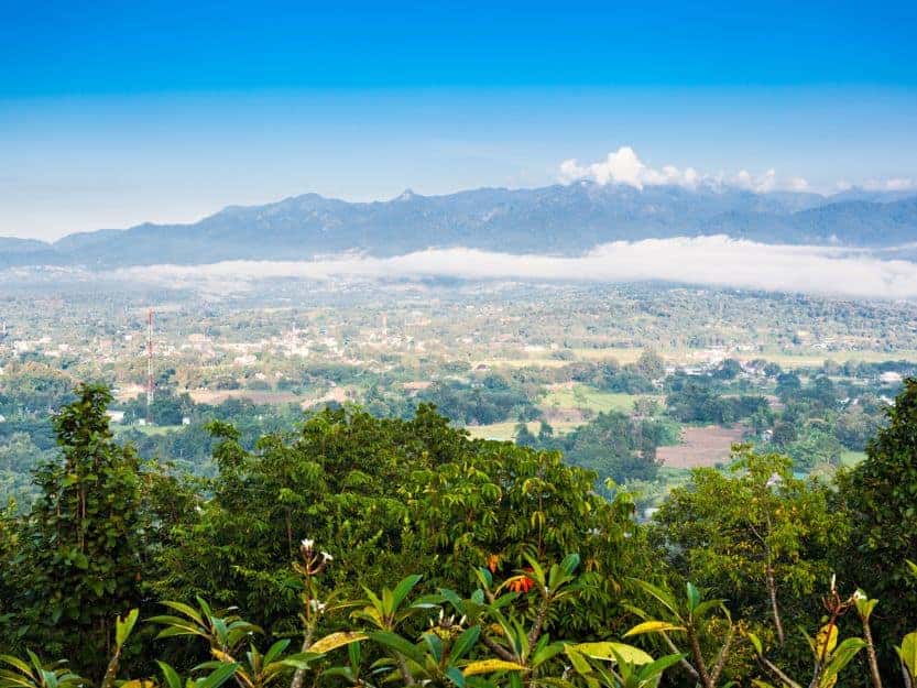 Aerial View of Pai in Thailand Aerial view of Pai in Thailand, with blue sky and cloud topped mountains in the background, then the village in front and vibrant green trees in the foreground.