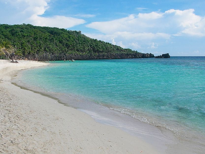 West Bay Beach on Roatan Island in Honduras West Bay Beach on Roatan Island in Honduras. White sandy bay beach on left with clear turquoise sea on the right with green tree covered hill in background.