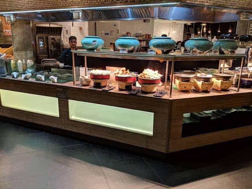 photo showing lots of serving bowls in the buffet full of foos and staff cooking in background