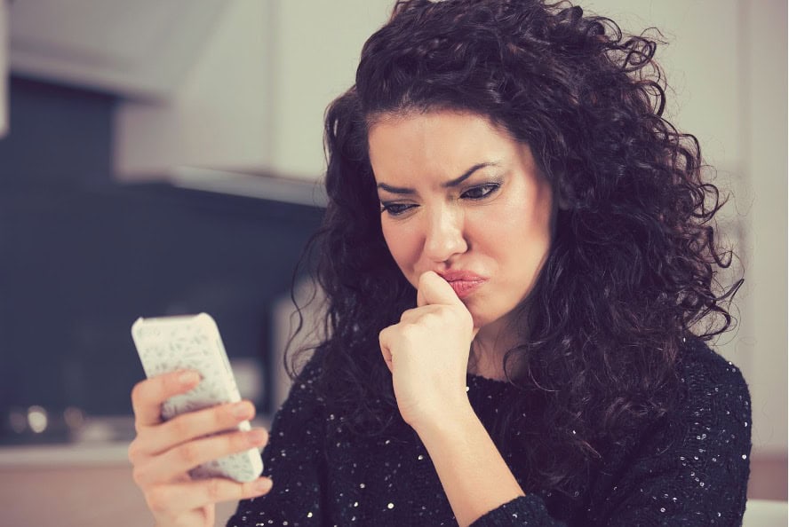 A curly-haired woman looking skeptically at her cell phone as she considers finding the right match.