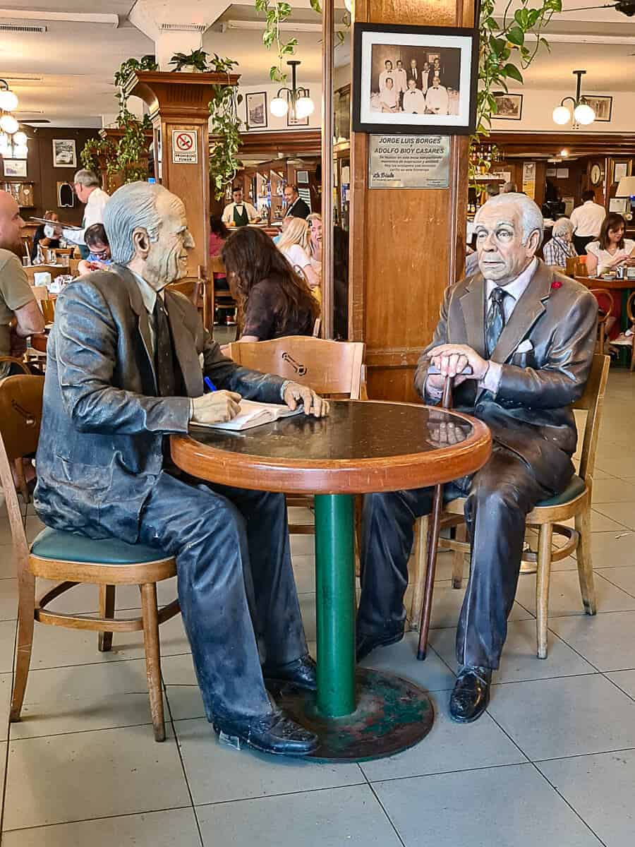 Statues of Jorge Luis Borges and Adolfo Bioy Casares at their reserved table inside La Biela Bar in Buenos Aires. This historic café in the Recoleta neighborhood is a hidden gem, offering a glimpse into the literary history of Argentina and a unique setting for enjoying traditional coffee and local culture.