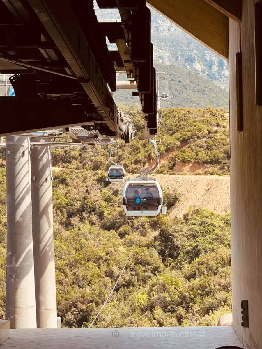 Cable cars approaching the station at the top of Mount Dajti, with a bird's eye view of trees and land below. A perfect addition to your sightseeing tour of Tirana on foot. 