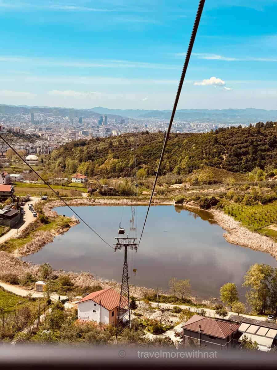 The view over a lake and trees as the Dajti Ekspres Cable Car climbs higher over Tirana. Your Tirana sightseeing walk should start or end here for maximum efficiency.
