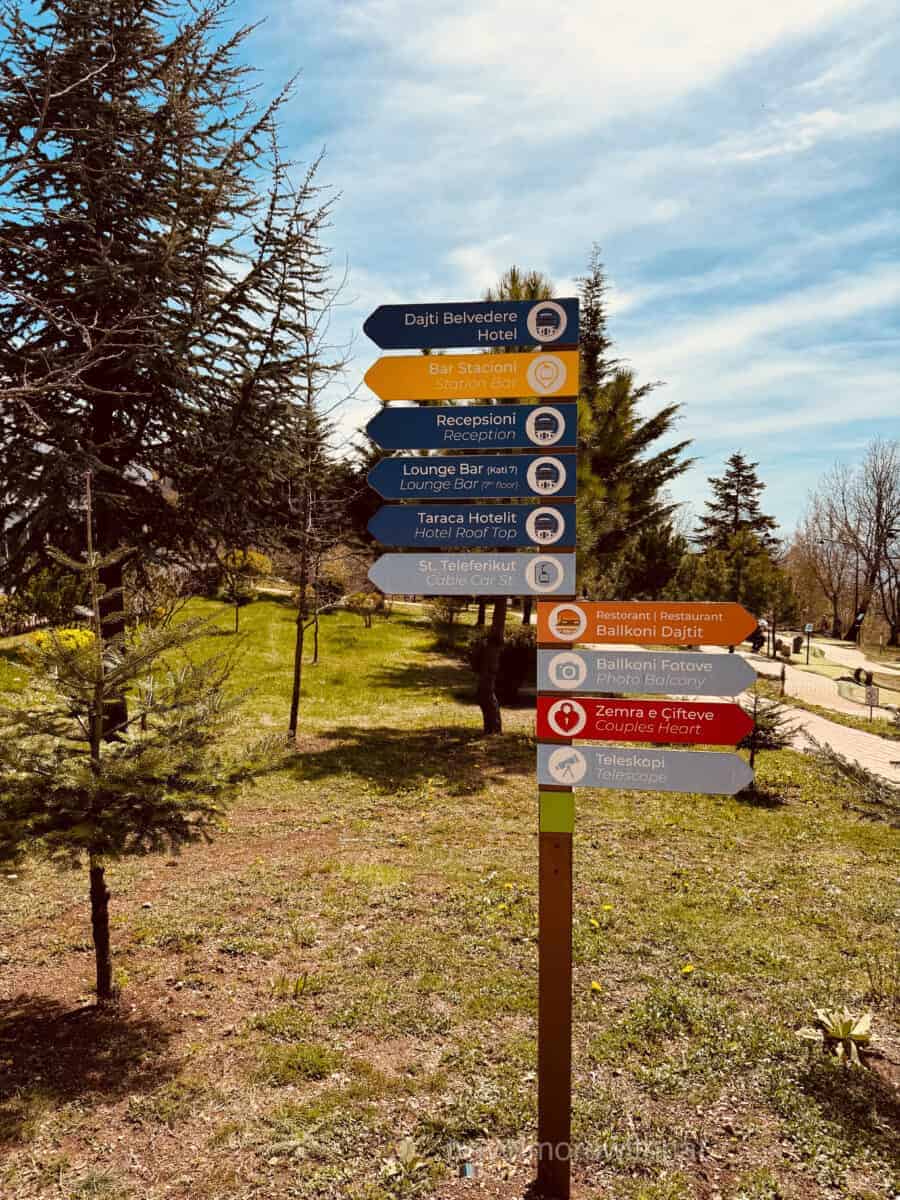 A signpost with multiple coloured arrows shows the sights at the top of Mount Dajti, where your self-guided tour of Tirana continues.