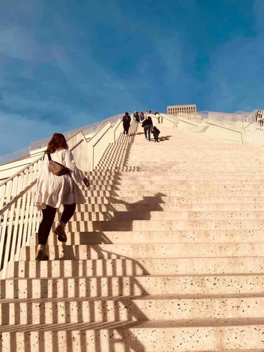 The sun casts shadows of the railings as a visitor climbs the steps on the exterior of Tirana Pyramid. A great way to explore Tirana on foot.