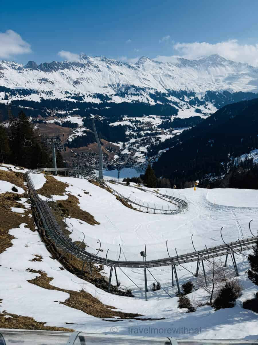 Snowy mountain landscape with a network of metal mountain coaster tracks winding down a hillside.