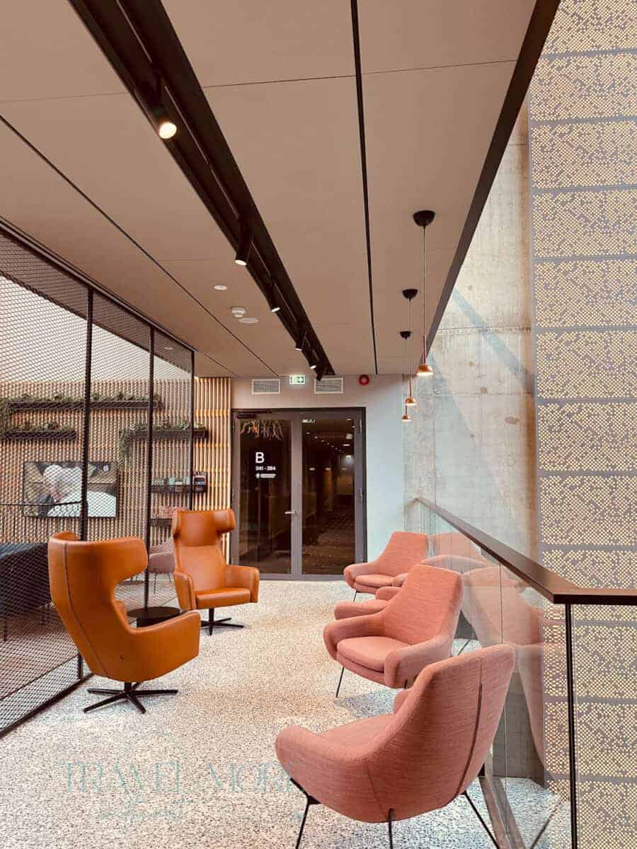A chic, modern lounge area at Citybox Tallinn with mid-century style chairs in soft pink and tan tones, set against minimalist decor and large windows. Ideal for solo female travellers seeking stylish, well-lit communal spaces in upscale accommodations.