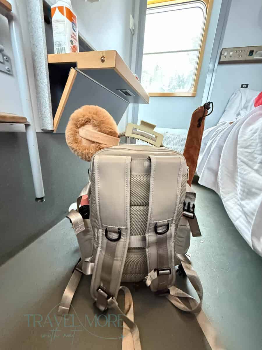 Small travel backpack placed on the floor of a compact hostel room beside a bed and desk. Choosing a compact bag helps travelers stay within airline hand luggage allowance limits.