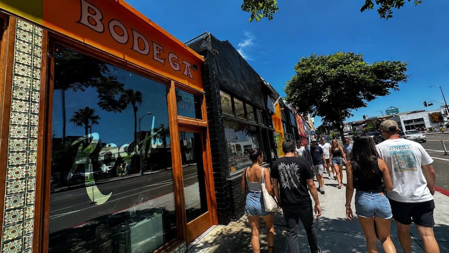 Groups of people walking along University Avenue past restaurants and local shops in North Park, San Diego, on a sunny day.