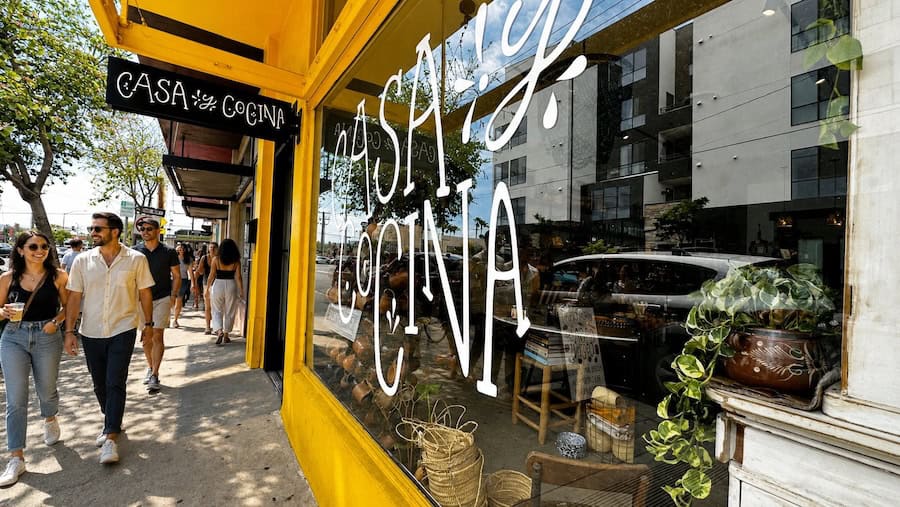 Happy groups of people walking along sunny Ray Street past the Casa y Cocina storefront in North Park, San Diego.