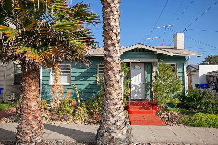 Charming teal Craftsman-style bungalow in North Park featuring a bright red walkway, white trim, and tall palm trees under a clear blue sky.