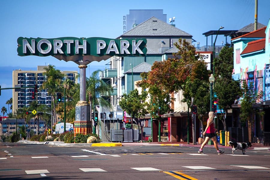 Woman walking her dog across the street in front of the North Park sign