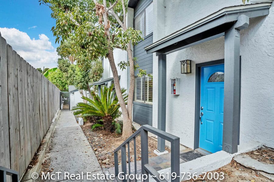 Gated side entrance featuring a concrete walkway, a bright blue front door under a grey portico, and low-maintenance tropical landscaping at 3711 Louisiana Street in North Park.