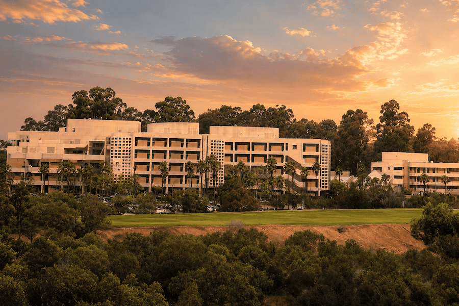 Naval Medical Center San Diego building viewed across a green lawn at warm sunset, surrounded by palm trees and taller trees.