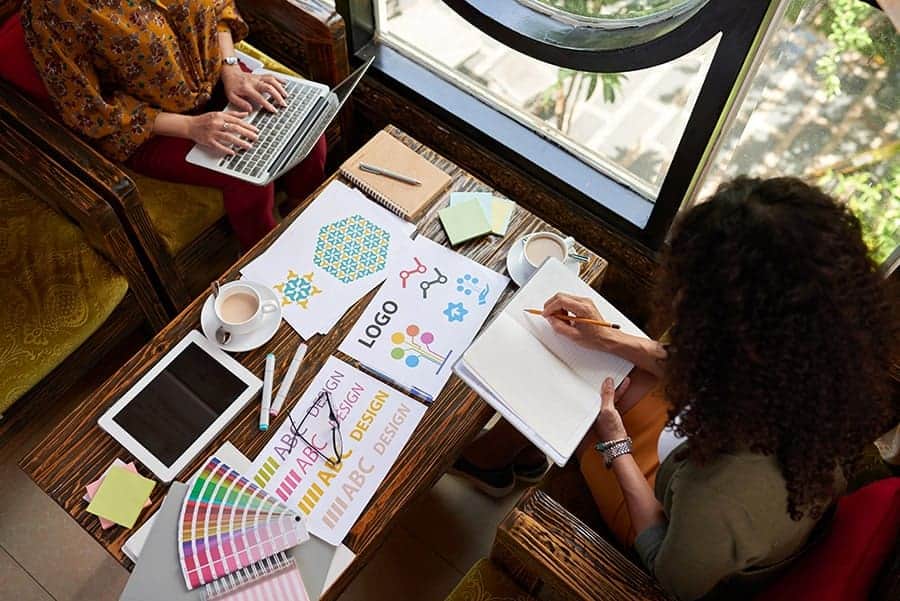 Creative team working on branding and design projects at a cozy office space in Switzerland, with digital devices, color swatches, and design sketches for innovative visual solutions.