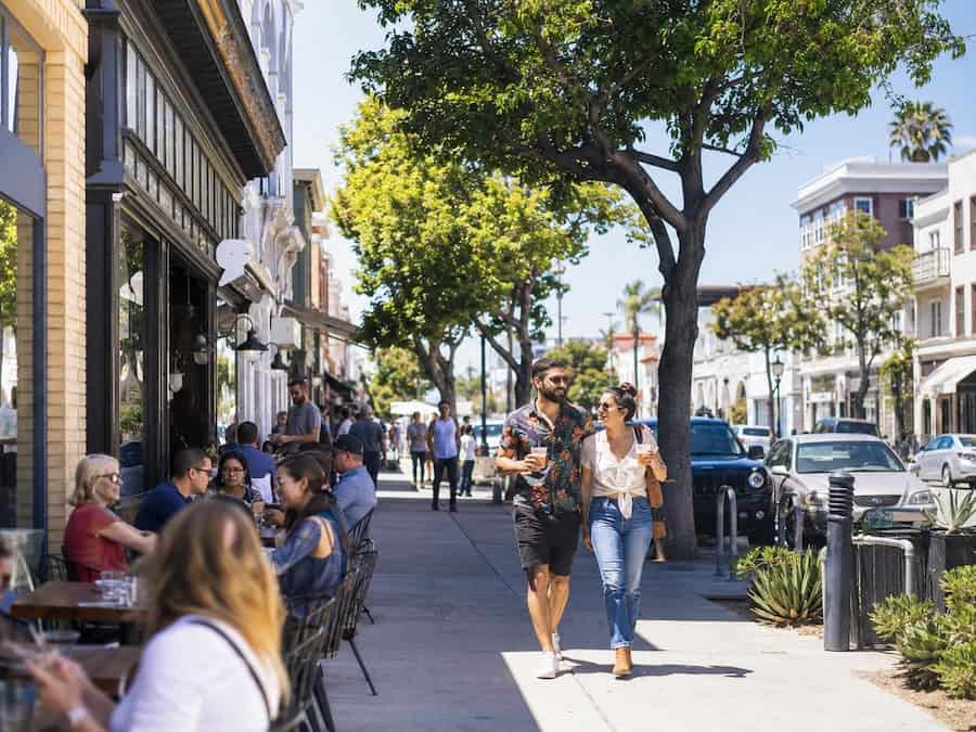Sunny North Park San Diego street scene with outdoor café seating, tree-lined sidewalks, local storefronts, and pedestrians enjoying the neighborhood’s walkable lifestyle.