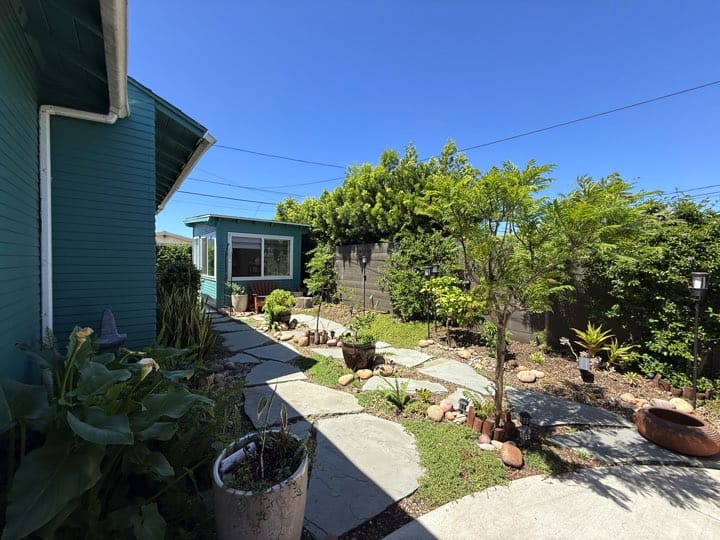 Landscaped backyard with a garden, mature trees, and a concrete walkway at a North Park San Diego home.