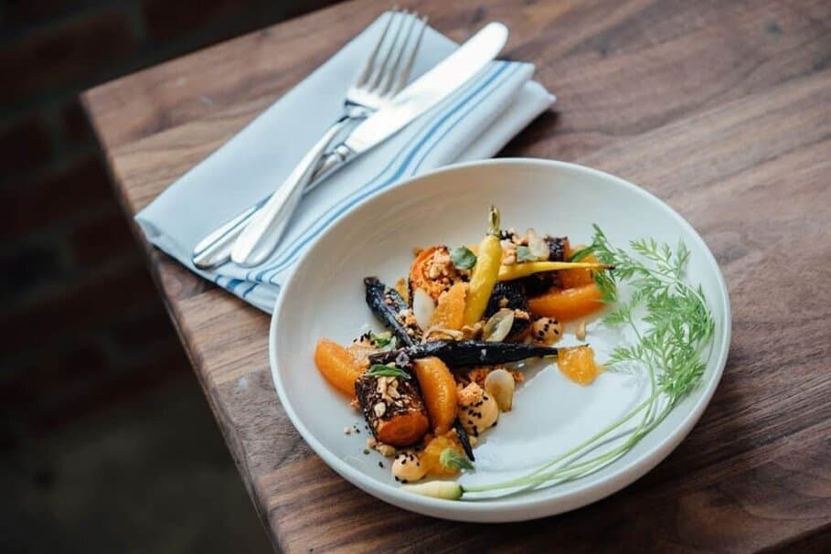 A fine dining plate of roasted glazed carrots with chopped nuts and citrus garnish, highlight the Best Dinner in Canterbury.
